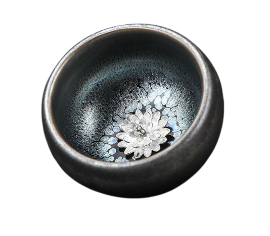 A silver teapot with a floral pattern on the inside, specifically a lotus flower design, and a dark, textured exterior.