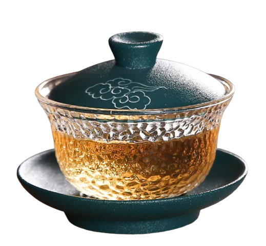 A clear and green colored crystal Gaiwan with a lid and a handle, filled with a golden-brown liquid, presumably tea.