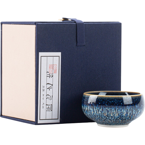 A beautifully crafted blue and white ceramic gift cup with a petal-shaped handle, presented in a sleek navy-colored box with Chinese characters and a golden lid.