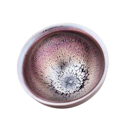 A tenmoku ceramic tea cup with a pink and black color pattern and a central dark spot.