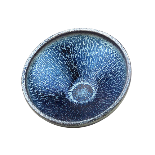 A blue tenmoku ceramic tea cup with a river-like pattern on the side.