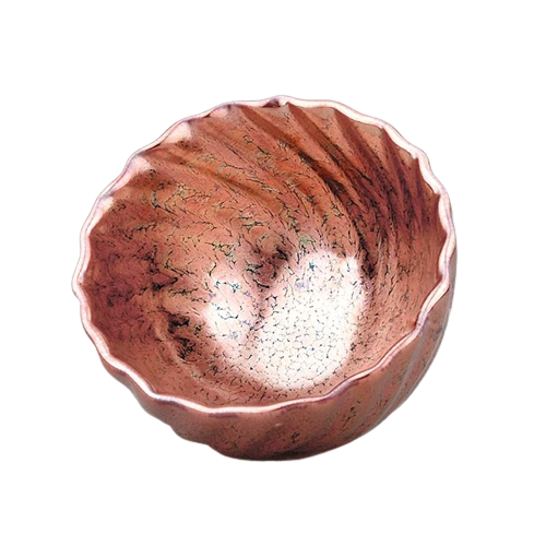 A rose gold colored ceramic tea cup with a textured surface, shown with a small amount of tea leaves inside.
