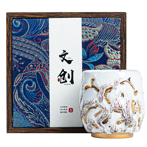 A white ceramic coffee cup with gold and red floral patterns, accompanied by a gift box with a traditional design.