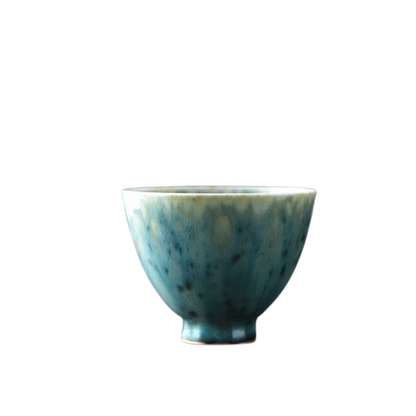 A ceramic tea cup with a gradient of green and blue colors on a dark background.