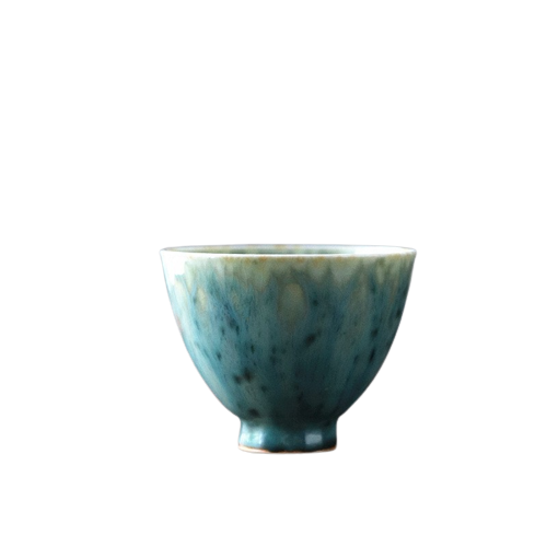 A ceramic tea cup with a gradient of green and blue colors on a dark background.
