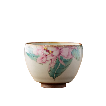 A painted ceramic tea cup with a floral design, predominantly pink and green, on a white background.