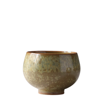 A ceramic tea cup with a beige and brown tenmoku (muddy) glaze.