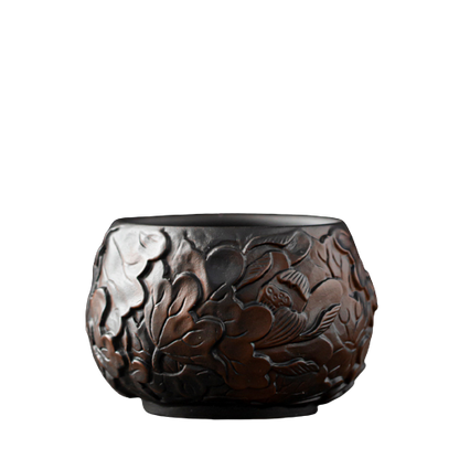 A black ceramic teapot with a floral pattern, resembling a lotus flower, on a plain background.