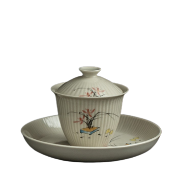A white and beige ceramic tea cup with floral patterns and a lid, placed on a matching saucer.