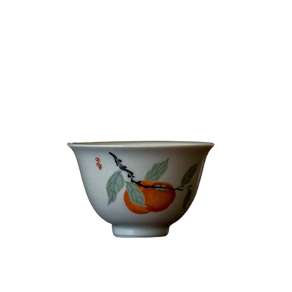 A white ceramic tea cup with a persimmon fruit design and leaf patterns around the rim.