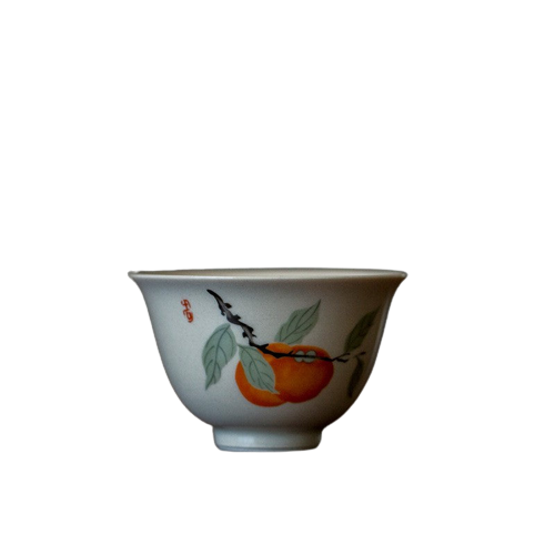 A white ceramic tea cup with a persimmon fruit design and leaf patterns around the rim.