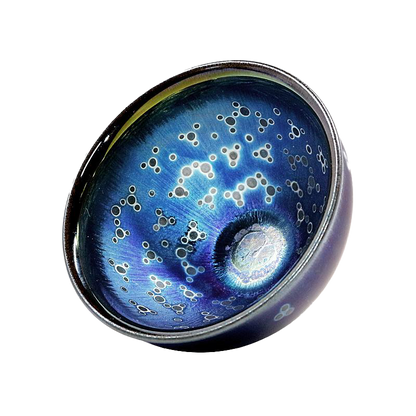 A circular ceramic tea cup with a blue color and a pattern of white dots or stars on the surface.