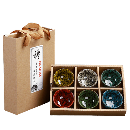 A set of six multicolored ceramic teacups in a gift box with a natural brown paper exterior and a decorative orange ribbon on top.