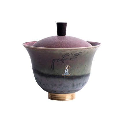 A round ceramic coffee cup with a purple and green color pattern and a gold-colored handle, featuring a tree and moon graphic on the side.