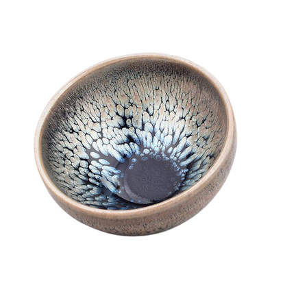 A round art ceramic tea cup with a swirling blue and gray Tenmoku glaze and a copperfield symbol in the center.