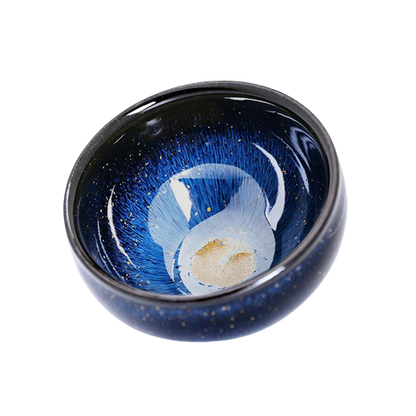 A blue and black ceramic tea cup with a floral pattern and a piece of tea leaf inside, showcasing the cup's color and design.