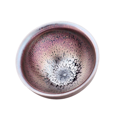 A tenmoku ceramic tea cup with a pink and black color pattern and a central dark spot.