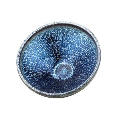 A blue tenmoku ceramic tea cup with a river-like pattern on the side.