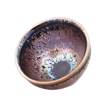 A round, high-temperature fired ceramic teapot with a mottled multicolor finish and a central, eye-like pattern.