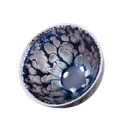 A ceramic tea cup with a blue and black sunrise-like pattern and a central metallic ring.