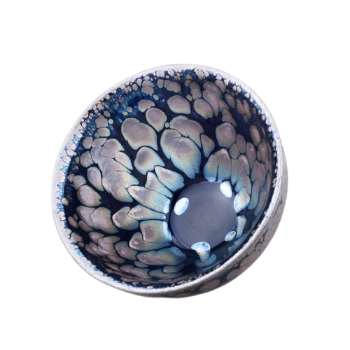 A ceramic tea cup with a blue and black sunrise-like pattern and a central metallic ring.